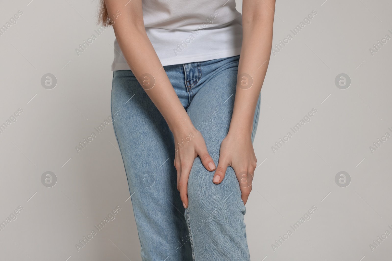 Photo of Woman suffering from pain in her knee on light grey background, closeup. Arthritis symptoms