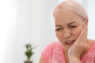 Mature woman suffering from strong tooth pain at home, space for text