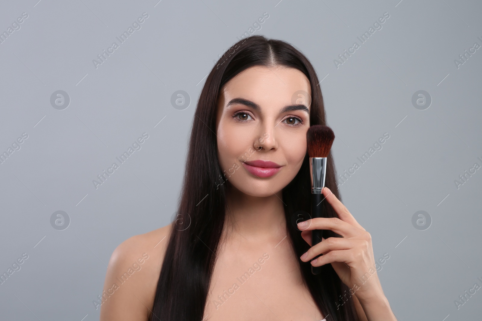 Photo of Beautiful woman with makeup brush on light grey background