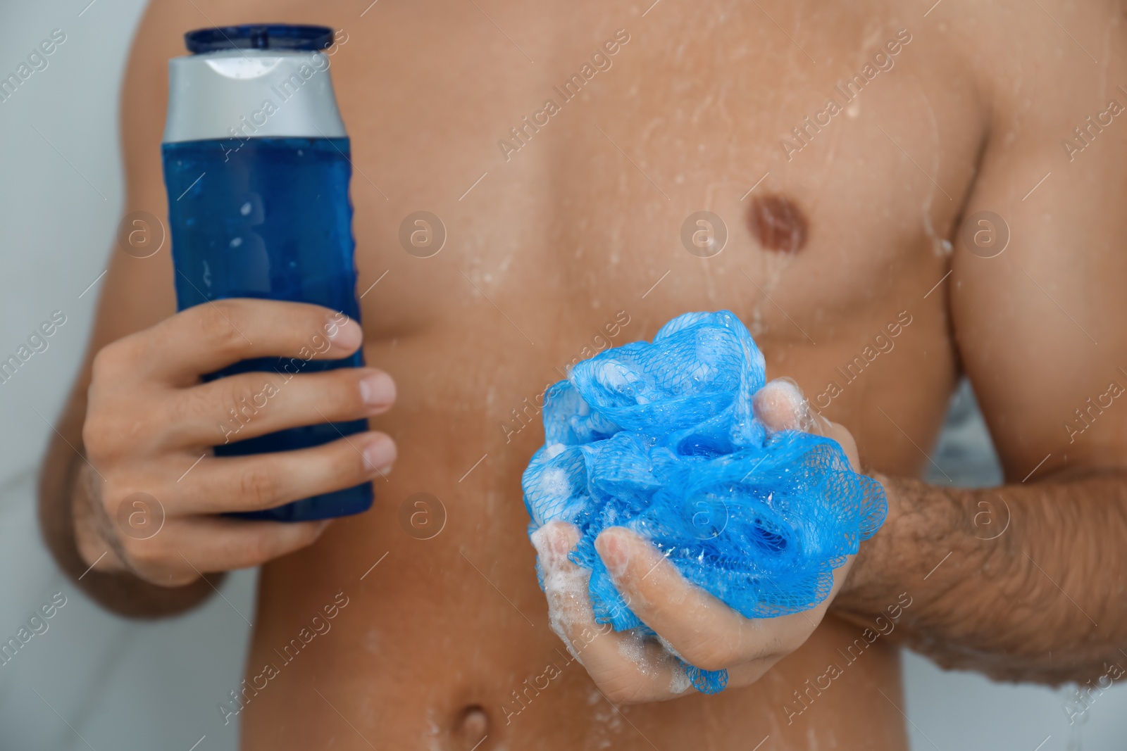 Photo of Man with bottle of gel and mesh pouf in shower at home, closeup