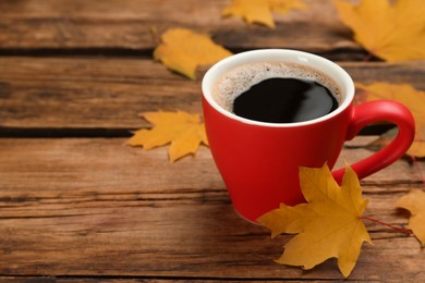 Cup of hot coffee and autumn leaves on wooden table, space for text