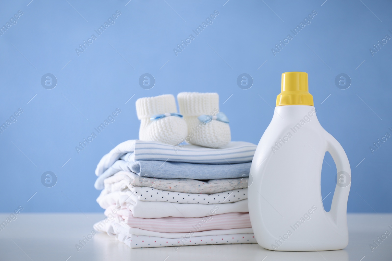 Photo of Detergent and children's clothes on white table near blue wall