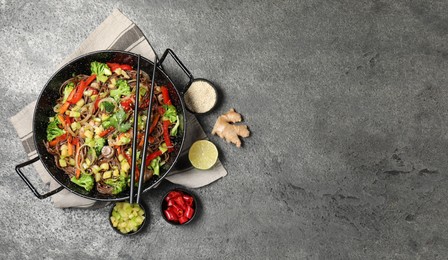 Photo of Wok with noodles, mushrooms, vegetables and other products on grey table, flat lay. Space for text