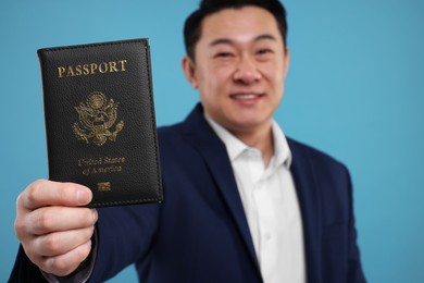 Photo of Immigration. Happy man with passport on light blue background, selective focus