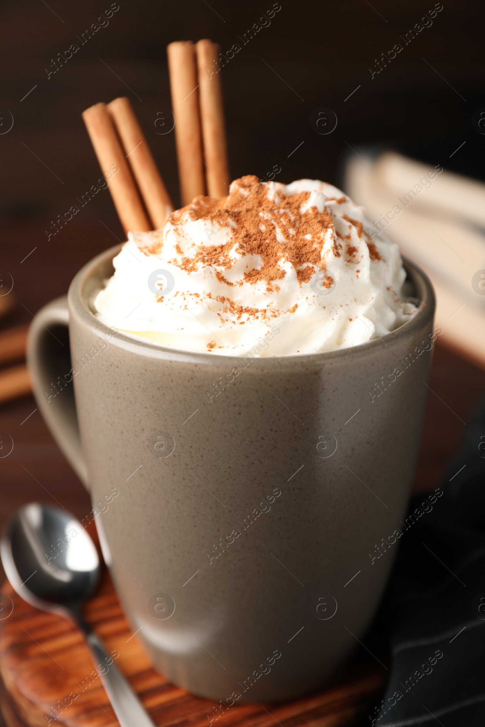 Photo of Cup of hot drink with aromatic cinnamon and whipped cream on wooden table, closeup
