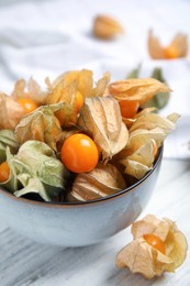 Photo of Ripe physalis fruits with dry husk on white wooden table, closeup