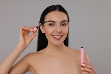 Photo of Beautiful young woman applying mascara on grey background