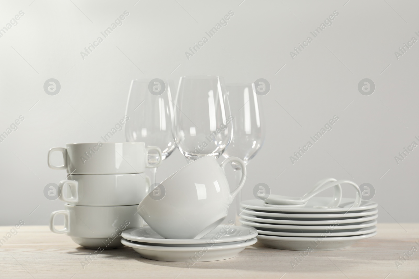 Photo of Set of clean dishware and glasses on white wooden table against light background