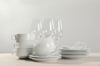 Set of clean dishware and glasses on white wooden table against light background