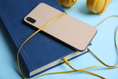 Book, modern headphones and smartphone on light blue background, closeup