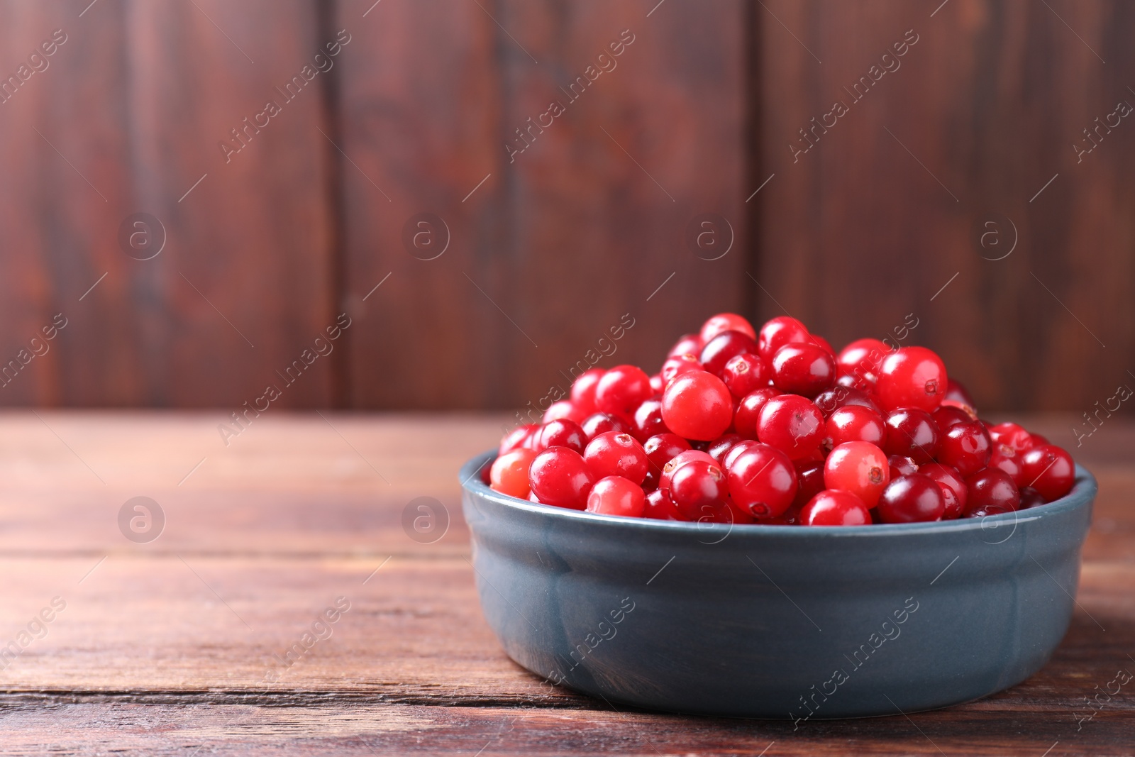 Photo of Fresh ripe cranberries in bowl on wooden table. Space for text