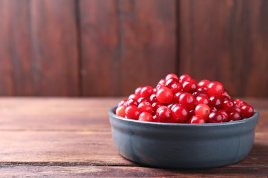 Photo of Fresh ripe cranberries in bowl on wooden table. Space for text