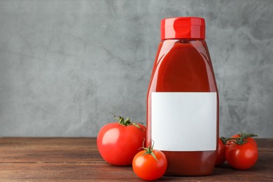 Photo of Bottle of tasty ketchup and tomatoes on wooden table. Space for text