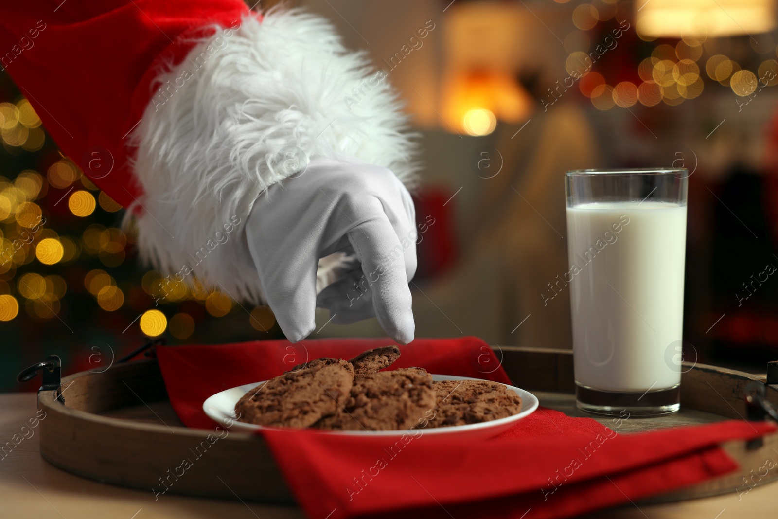 Photo of Merry Christmas. Santa Claus taking cookies from plate on table in room, closeup