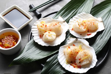 Photo of Raw scallops with spices, lemon zest, shells and sauces on grey textured table, closeup