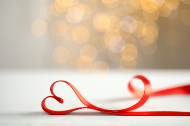 Photo of Heart made of red ribbon on table against blurred festive lights, space for text. Valentine's day celebration