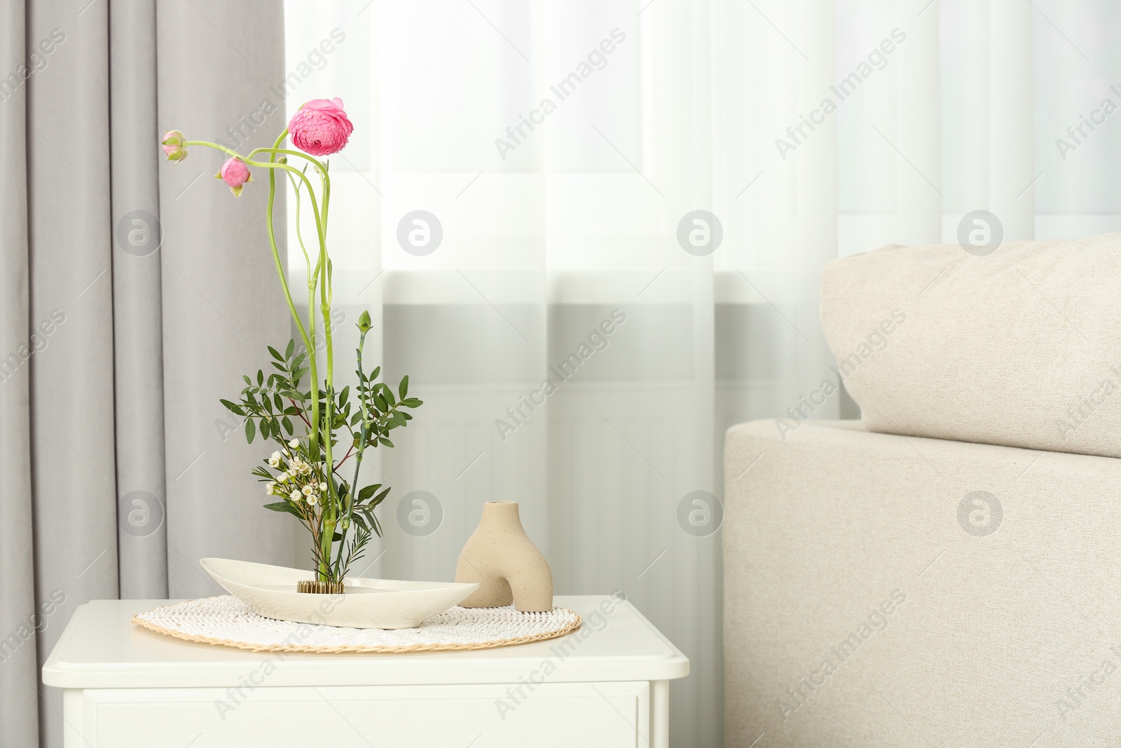 Photo of Ikebana art. Beautiful flowers and green branches carrying cozy atmosphere at home