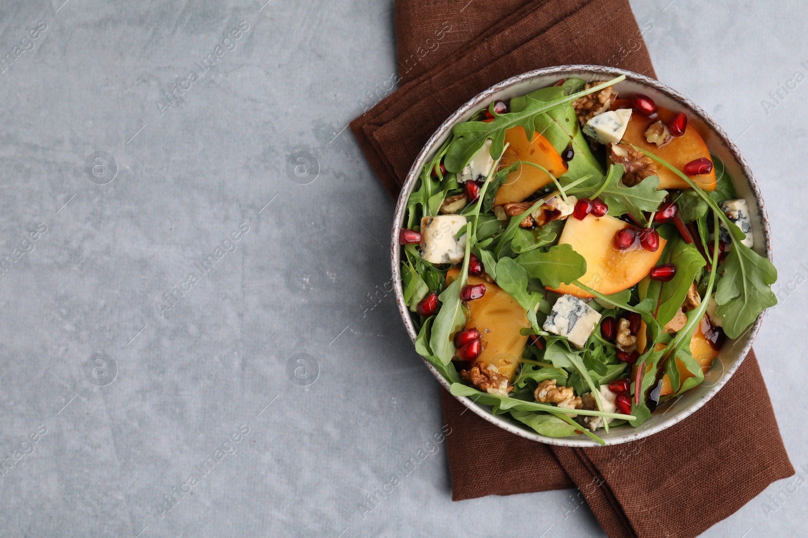 Photo of Tasty salad with persimmon, blue cheese, pomegranate and walnuts served on light grey table, top view. Space for text
