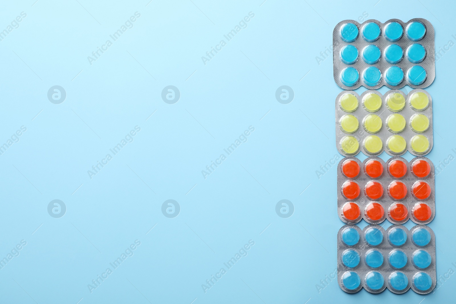 Photo of Blisters with colorful cough drops on light blue background, flat lay. Space for text