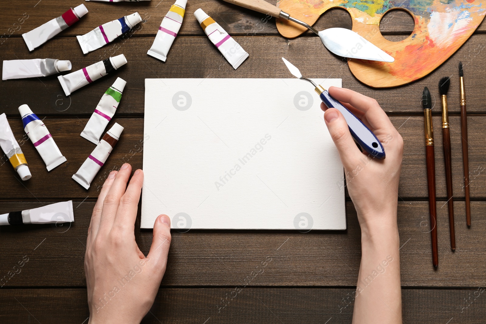 Photo of Man with spatula and blank canvas at wooden table, top view