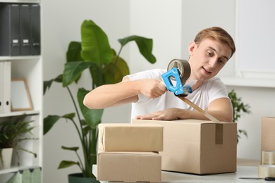 Photo of Young man packing box with adhesive tape indoors
