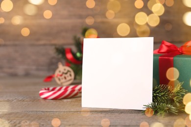 Photo of Blank Christmas card, gift box and fir branches on wooden table, space for text