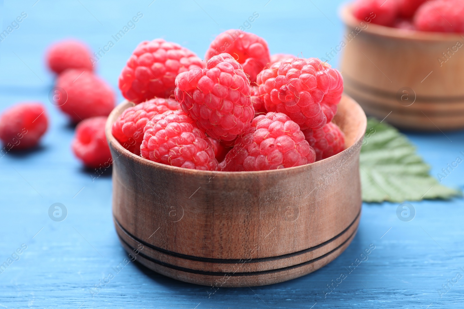 Photo of Delicious fresh ripe raspberries in bowl on blue wooden table