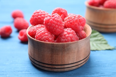 Photo of Delicious fresh ripe raspberries in bowl on blue wooden table