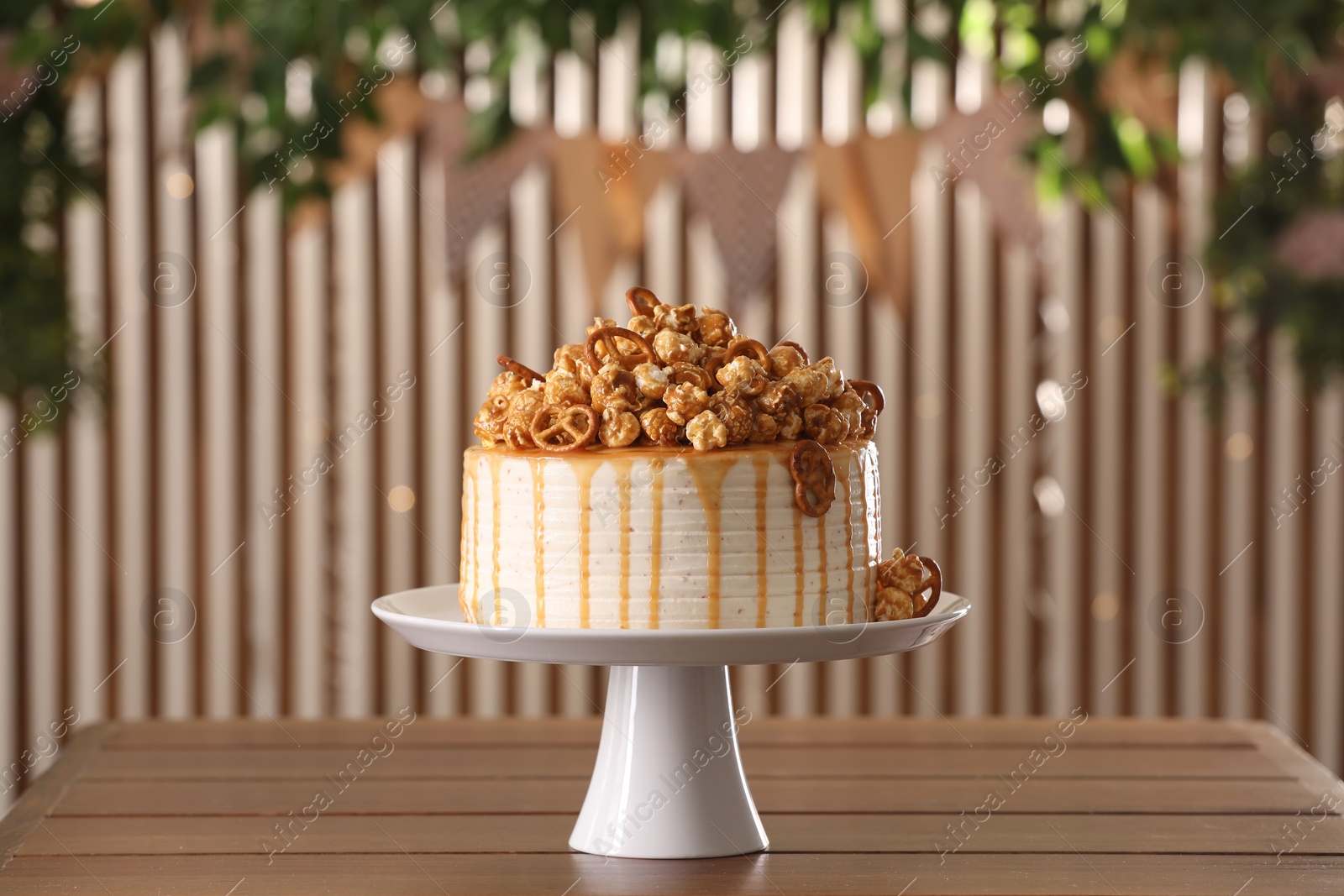 Photo of Caramel drip cake decorated with popcorn and pretzels on wooden table