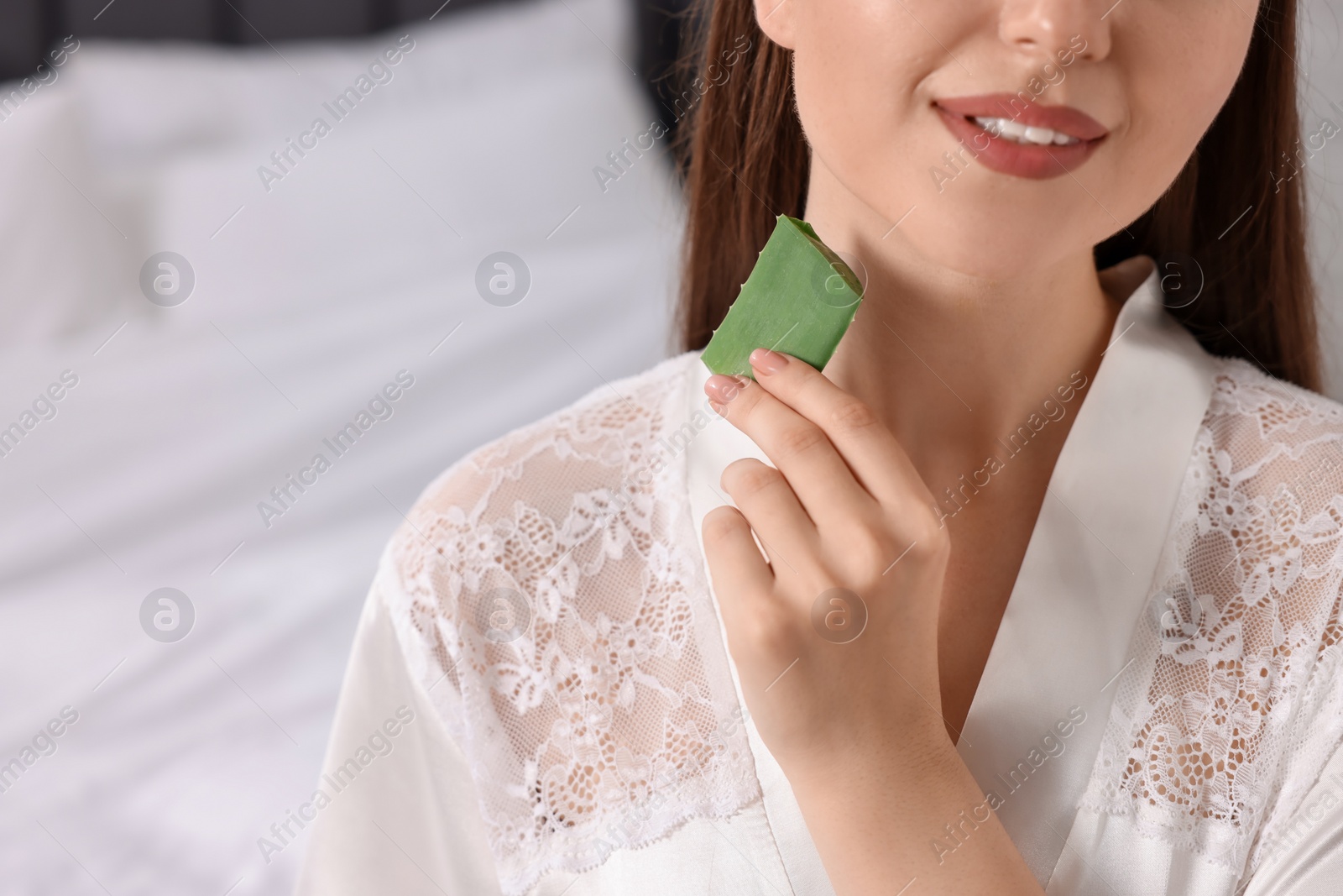 Photo of Young woman applying aloe gel from leaf onto her neck indoors, closeup. Space for text