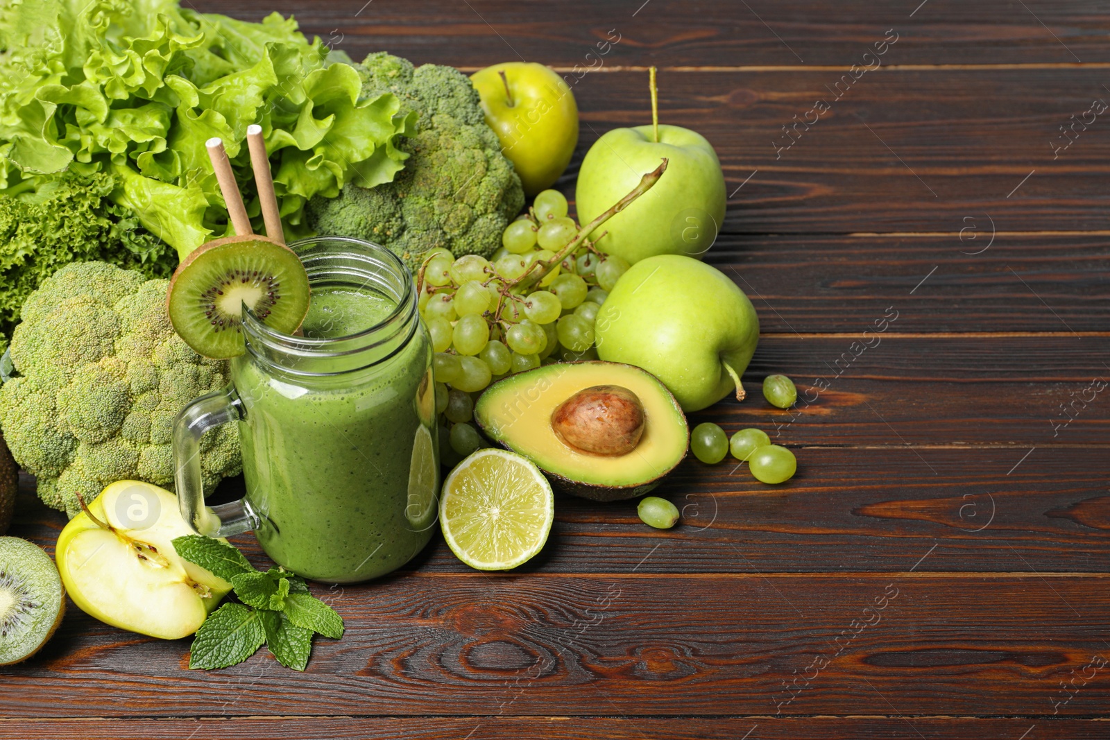 Photo of Green smoothie in mason jar and fresh ingredients on wooden table. Space for text