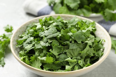 Cut fresh green cilantro in bowl on light grey table, closeup