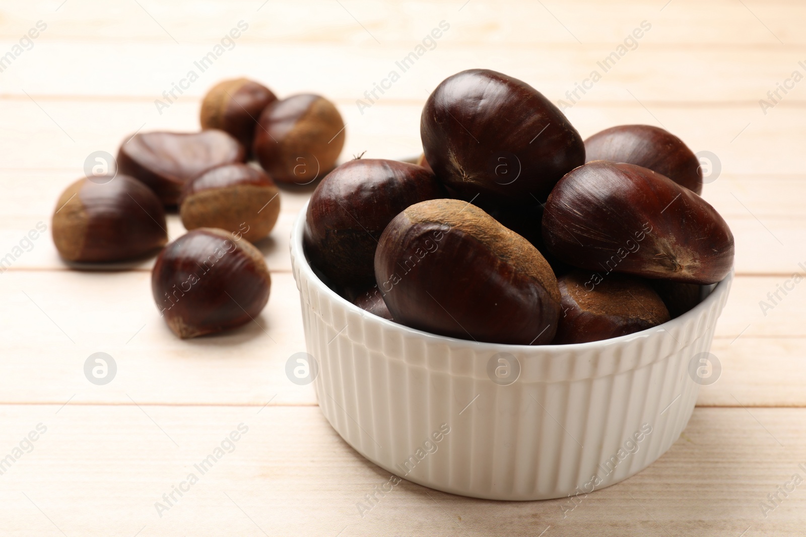 Photo of Sweet fresh edible chestnuts on light wooden table, closeup