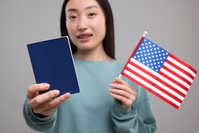 Photo of Immigration to United States of America. Woman with passport and flag on grey background, selective focus
