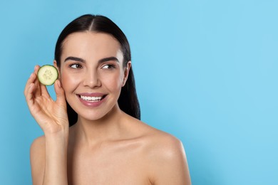 Photo of Woman holding piece of cucumber on light blue background, space for text. Spa treatment