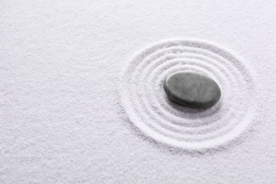 Photo of Zen garden stone on white sand with pattern, above view. Space for text