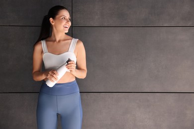 Photo of Smiling woman in sportswear with thermo bottle near dark grey wall. Space for text