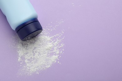 Bottle and scattered dusting powder on lilac background, top view with space for text. Baby cosmetic product