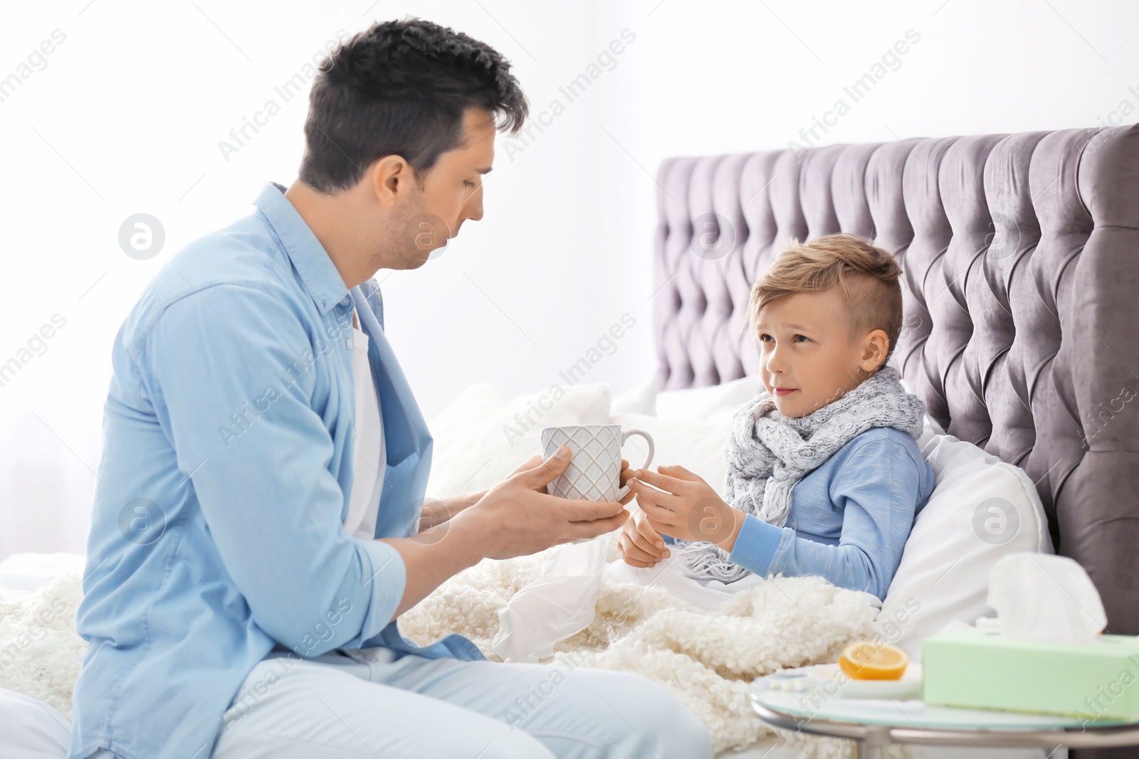 Photo of Father taking care of little son suffering from cold in bed