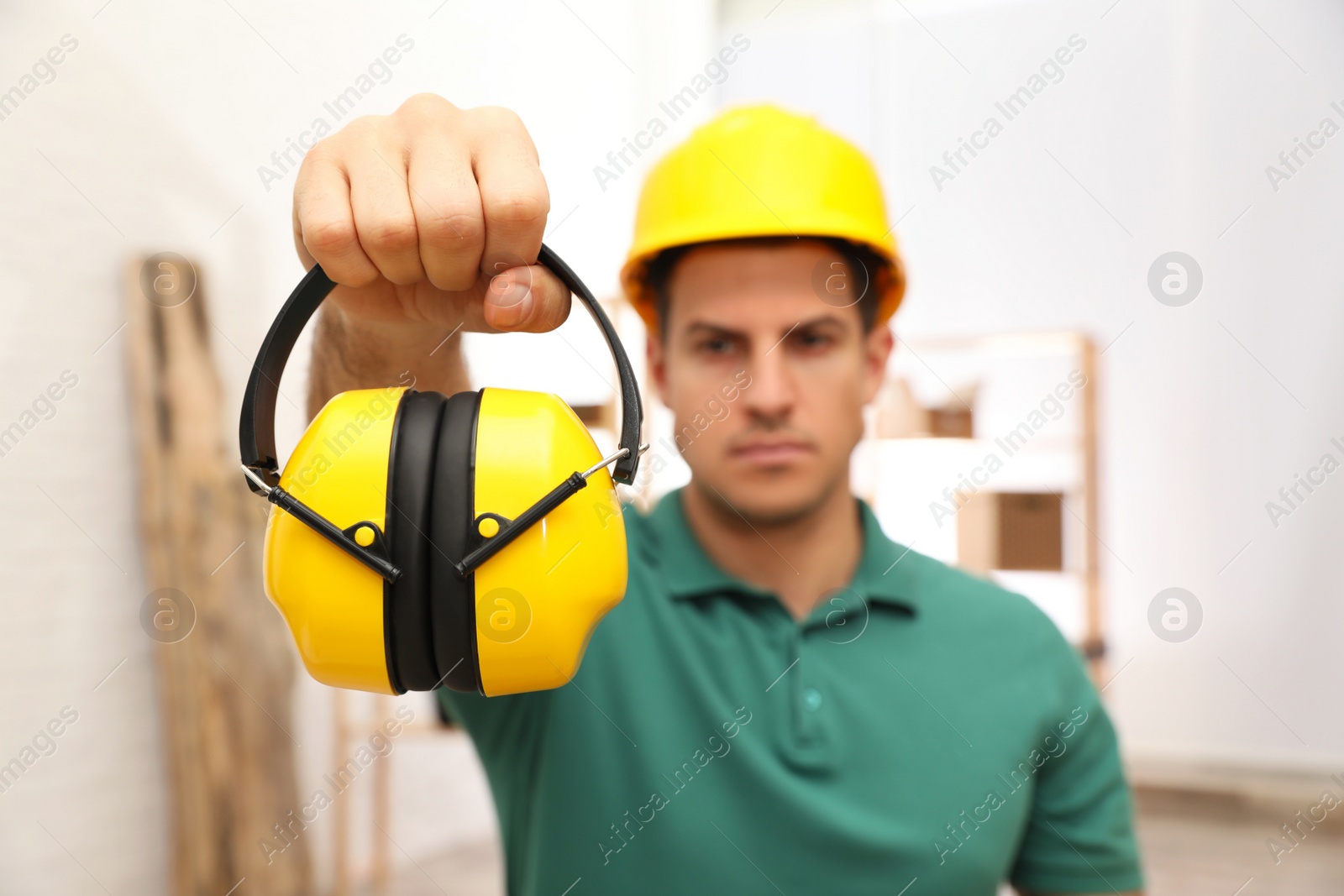 Photo of Worker holding safety headphones indoors, focus on device. Hearing protection