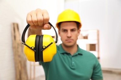 Photo of Worker holding safety headphones indoors, focus on device. Hearing protection