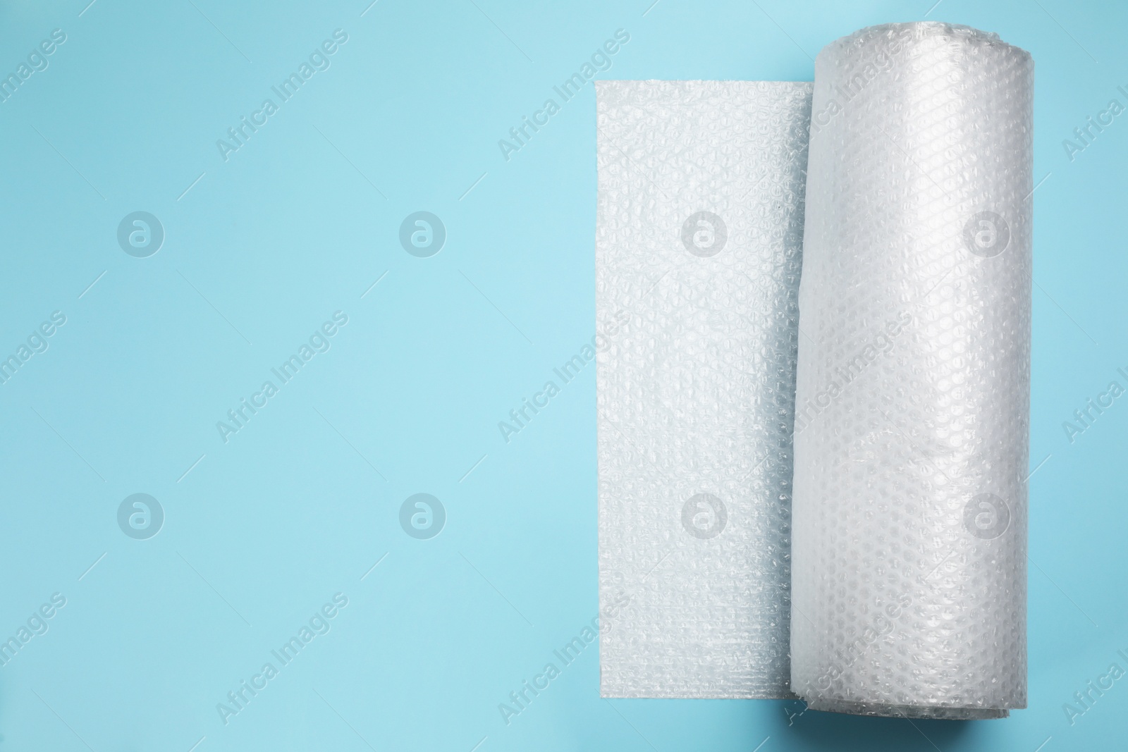 Photo of Bubble wrap roll on turquoise background, top view. Space for text