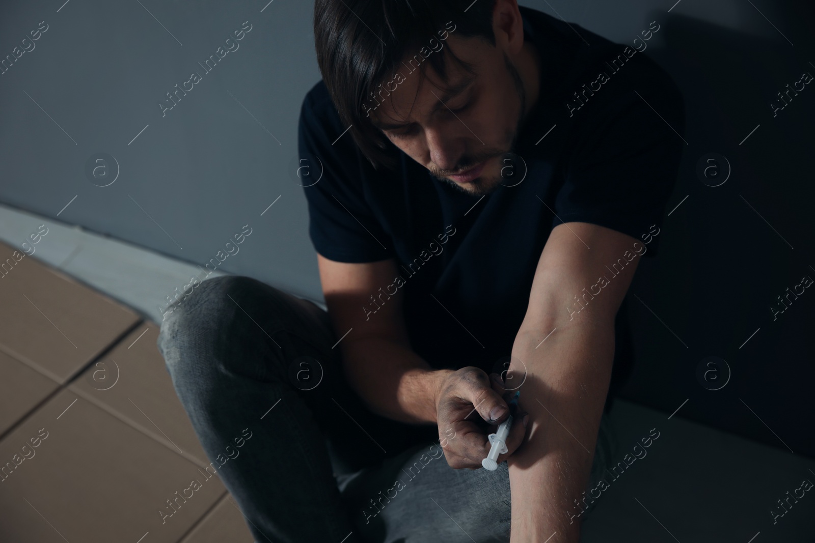 Photo of Male drug addict making injection near grey wall