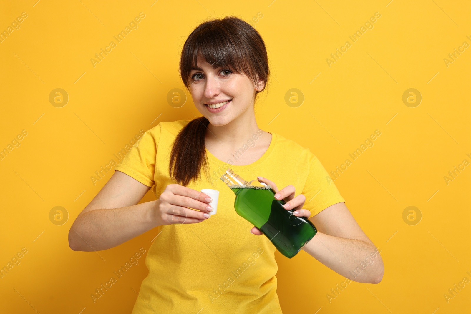 Photo of Young woman using mouthwash on yellow background