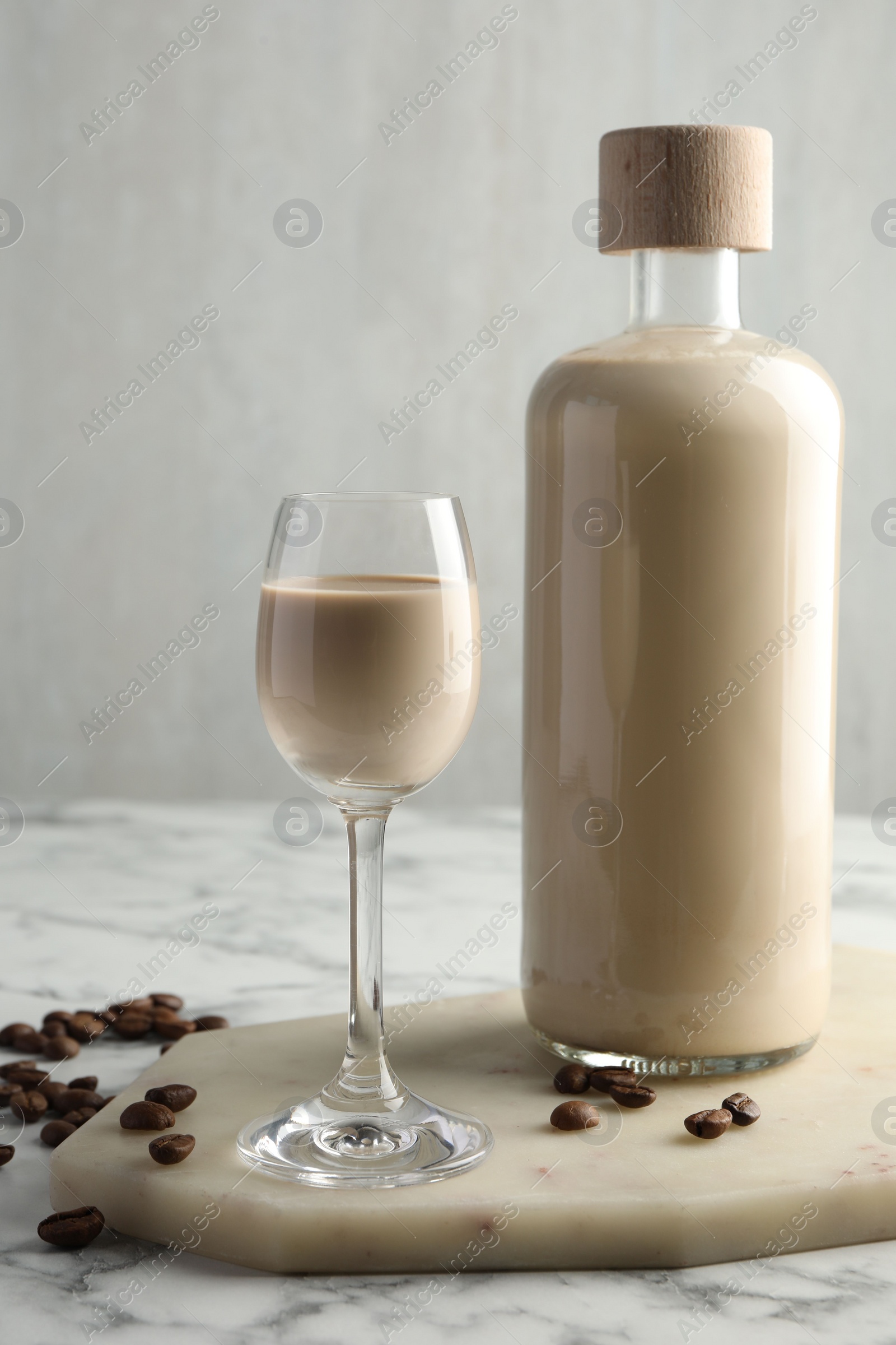 Photo of Coffee cream liqueur in glass, beans and bottle on white marble table