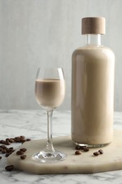 Coffee cream liqueur in glass, beans and bottle on white marble table