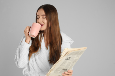 Photo of Beautiful young woman in bathrobe with cup of coffee on light grey background