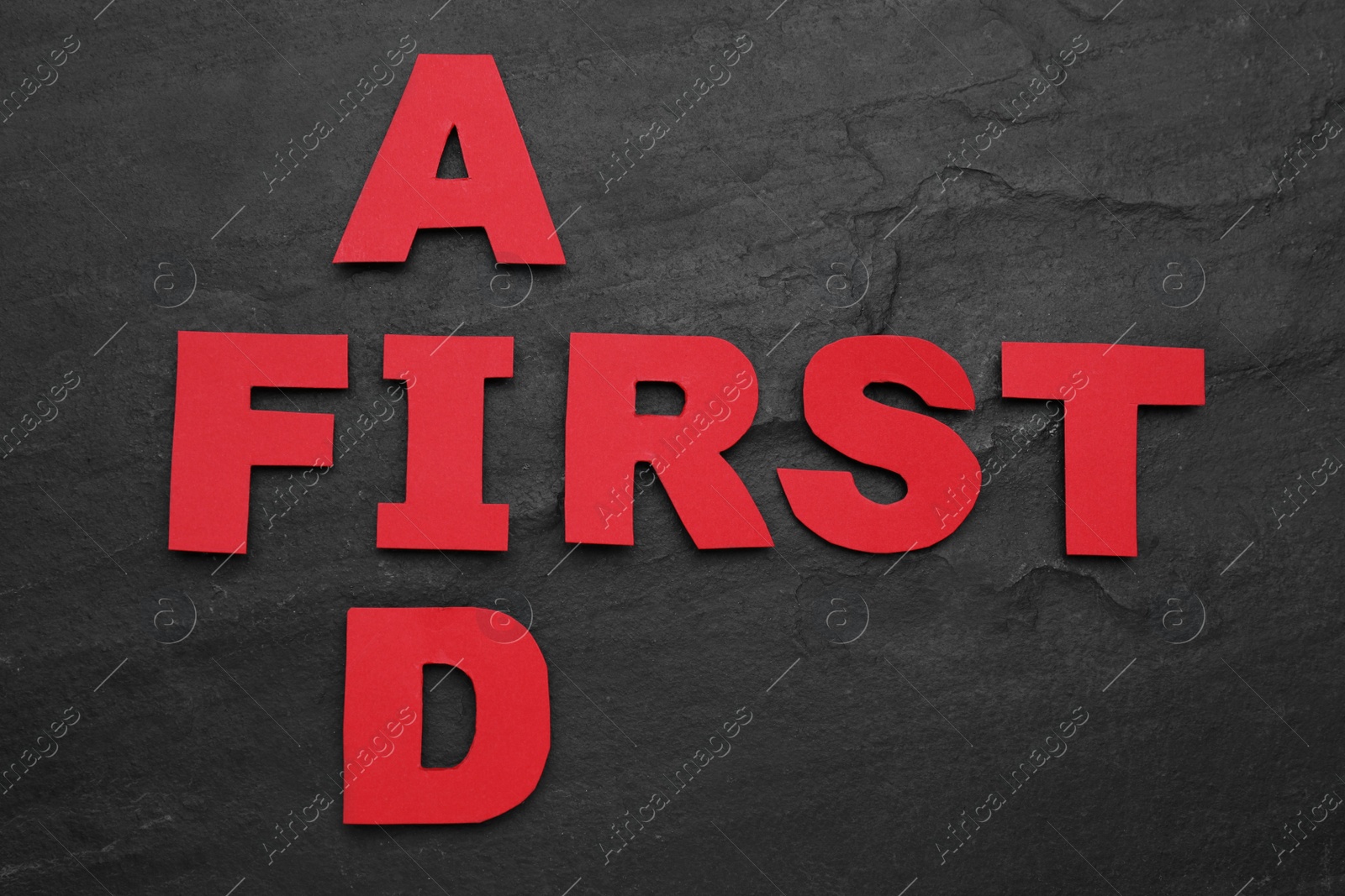 Photo of Words First Aid made of red letters on black table, flat lay