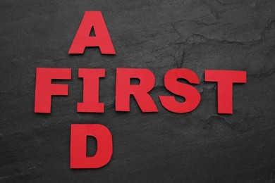 Photo of Words First Aid made of red letters on black table, flat lay