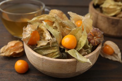 Ripe physalis fruits with calyxes in bowl on wooden table, closeup